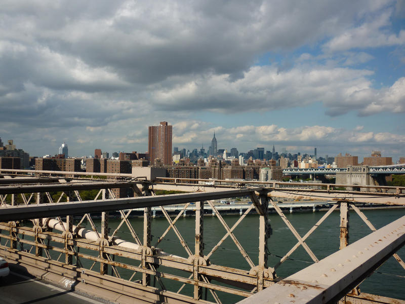 View of the steel frame of the historical landmark of Brooklyn bridge with the cityscape of Manhattan visble beyond under a cloudy sky