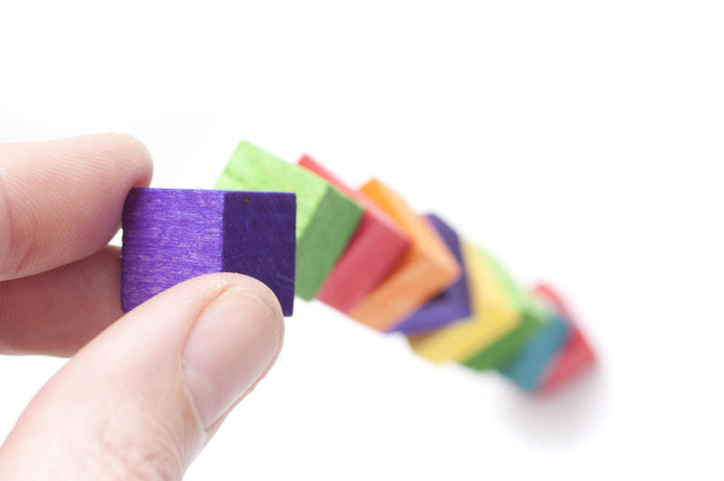 Male fingers building with colourful toy wooden blocks in a concept of development and expansion, or as a learning tool to teach kindergarten children coordination