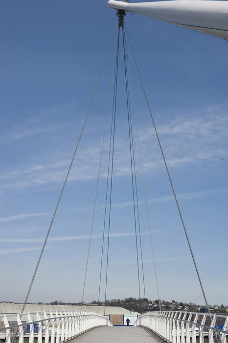 View across the span of newport City Footbridge which crosses the River Usk to a person in the distance showing the suspension cables