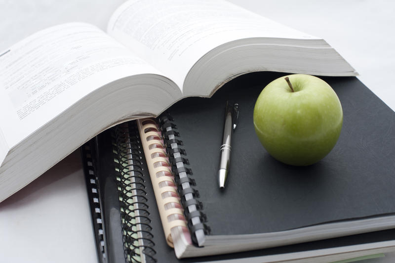 Conceptual background for education and college studies with a large open textbook alongside spiral bound notebooks and a pencil topped with a fresh healthy green apple