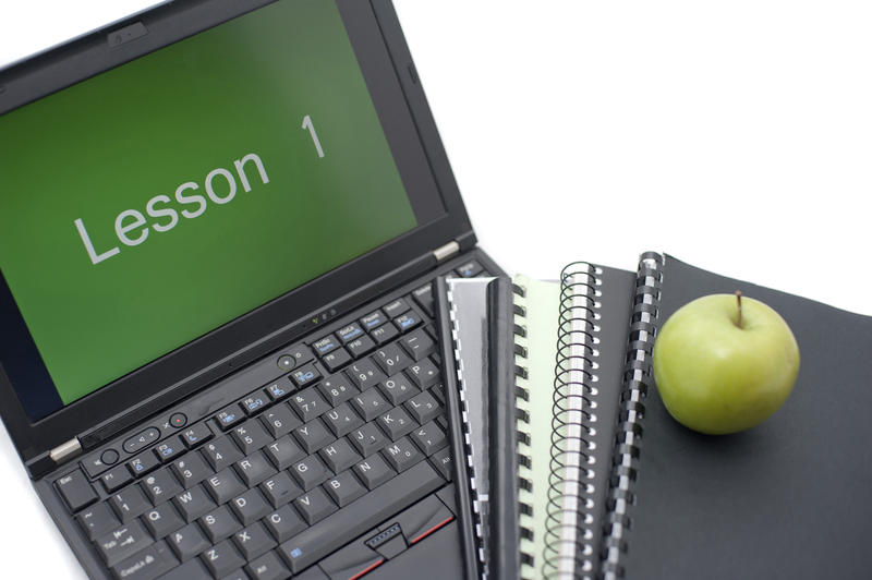 Computer training and learning concept with an open laptop with the words Lesson 1 viewable on the screen alongside spiral bound notebooks and an apple