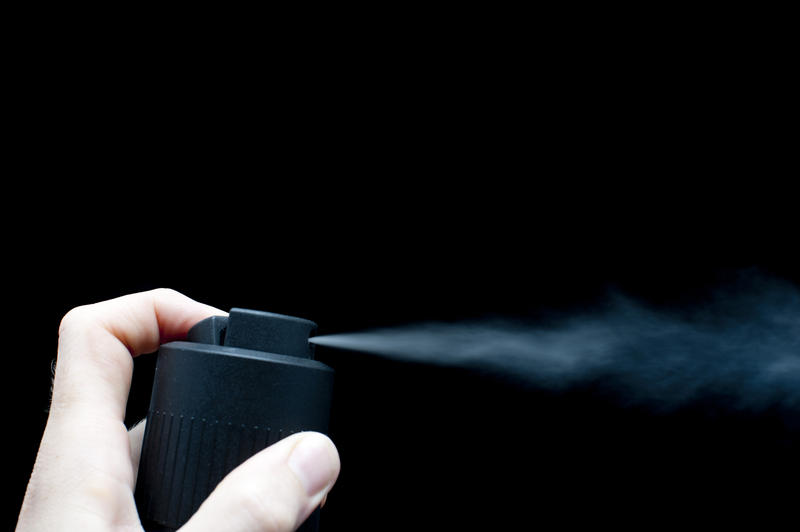 Man using a plain black spray can depressing his finger to emit a fine burst of vapour over black