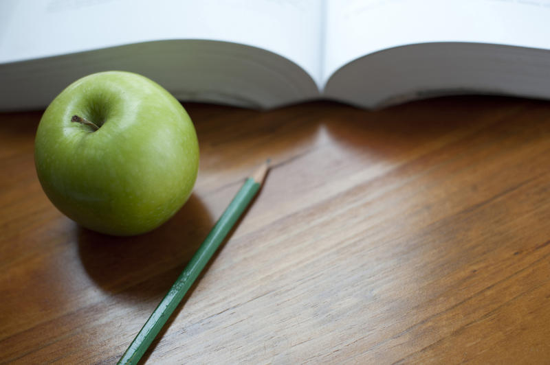 Table top with open book, a pencil and a green apple