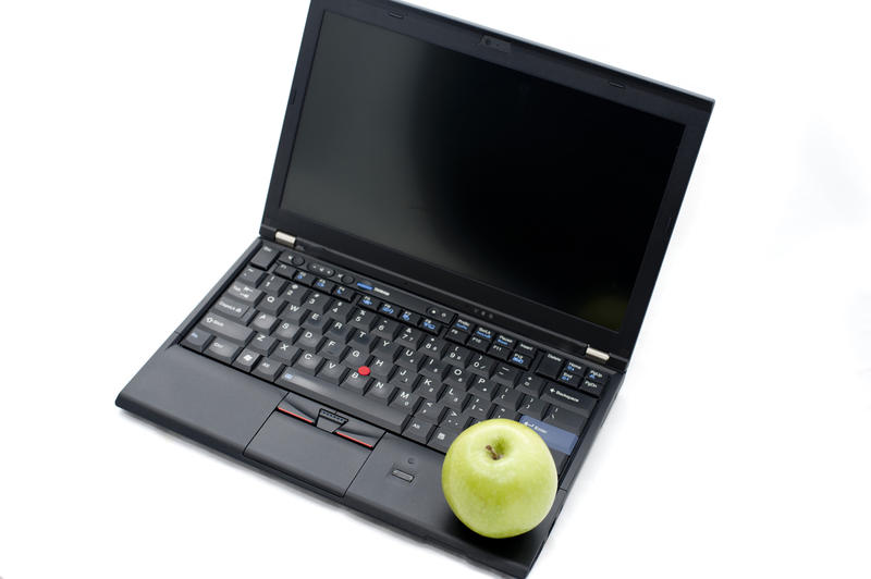E-learning or computer learning concept with an open laptop with a blank screen topped by fresh green healthy apple over white