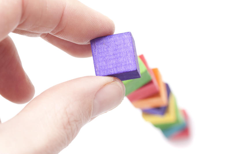 Hand building a tower of colourful wooden toy blocks conceptual of growth and development through learning and education