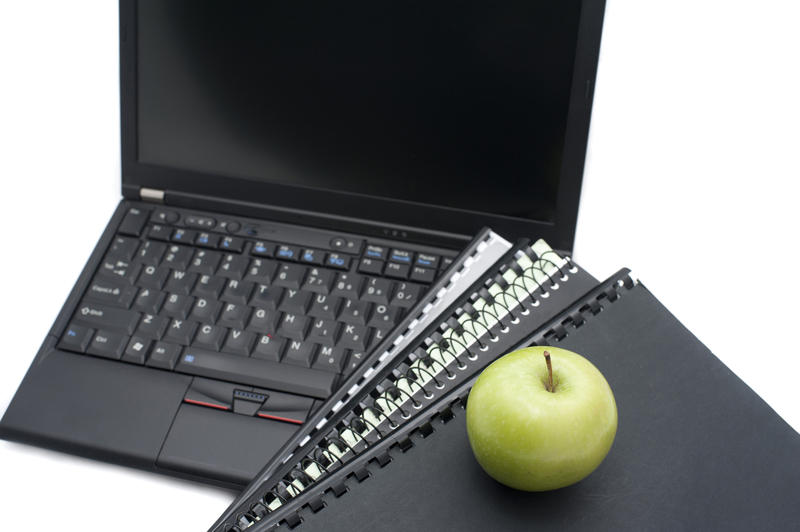 E-learning conceptual background with an open laptop with a blank screen alongside spiral bound notebooks and a healthy fresh green apple