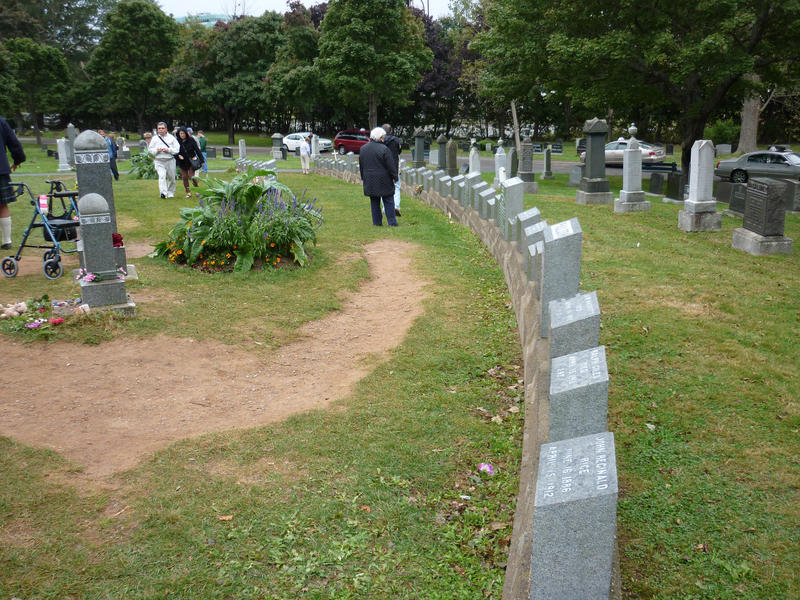 Row of Titanic gravestones at Fairview Lawn Cemetry where over 100 victims of the sinking are buried with people and cars in the background