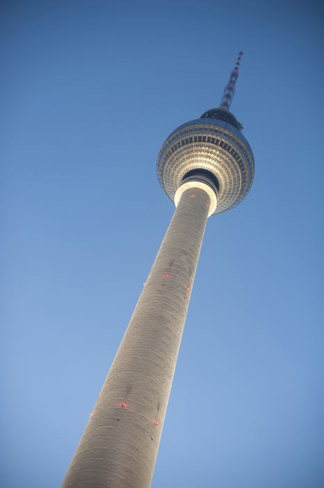 Looking up at the illuminated Alexanderplatz Tower in Berlin, Germany, with blue sky behind