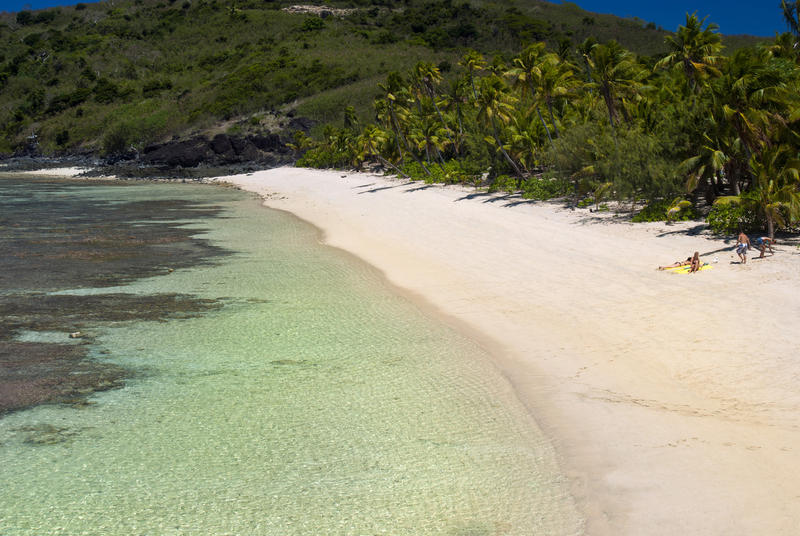 Idyllic Fiji beach with gently curving golden sand, crystal clear water and a fringe of lush green vegetation and palm trees