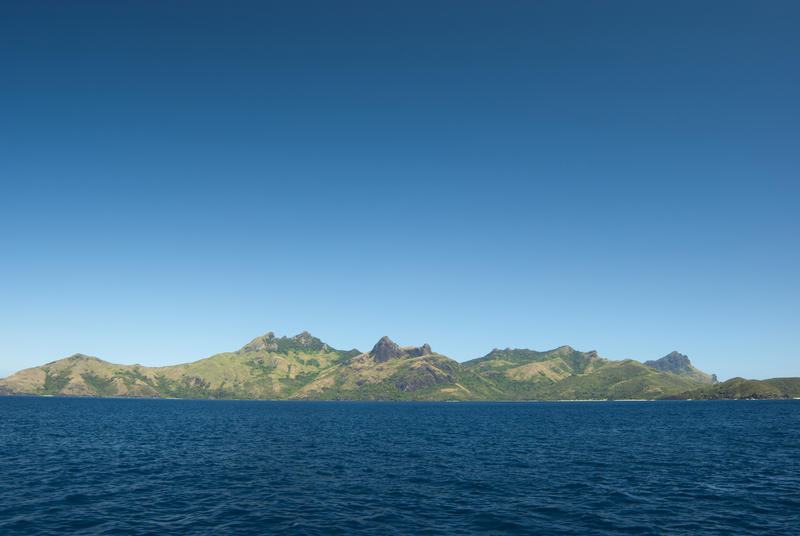 Ocean view from a passing boat showing the topography of the Fijian islands with their rocky hills, lush vegetation and golden sandy beaches