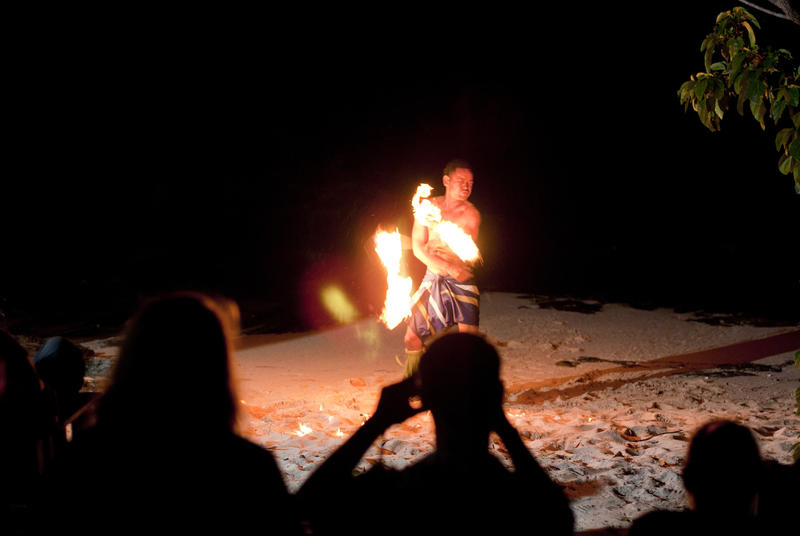 Tourists watching Fijian fire dancers perform on the beach swirling burning branches around in the air