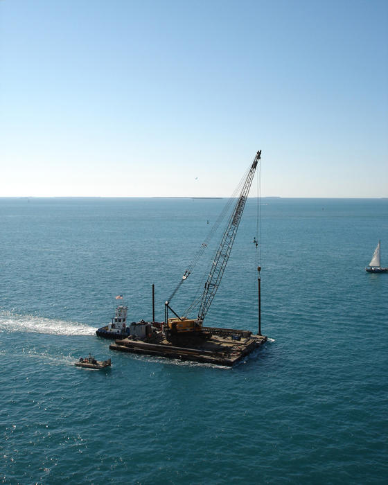 Huge floating crane on a platform being accompanied on its ocean voyage to a new site by tugs