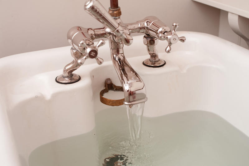 Partial view of a bathtub with running water from an old-fashioned faucet