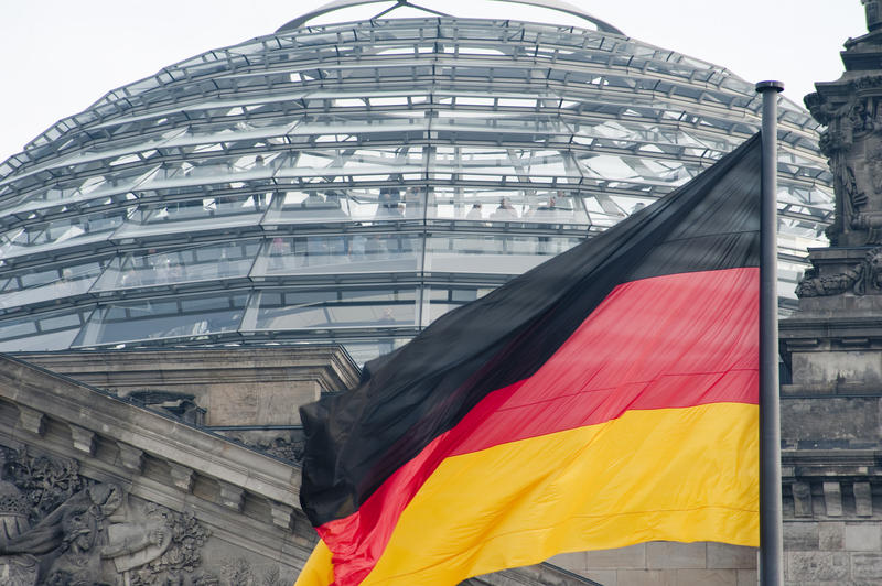 The German flag flying on a flagpole in front of the glass dome of the Reichstag building, Berlin, Germany