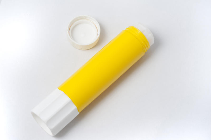 Yellow glue stick lying opened on its side on a white studio background