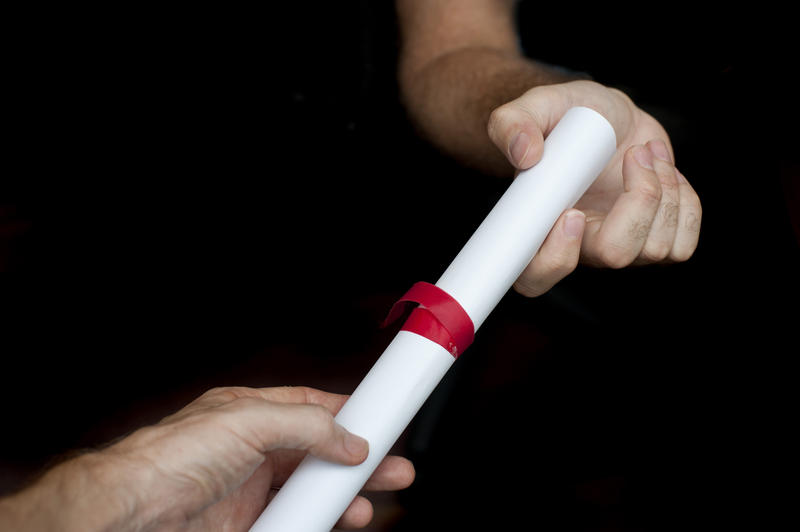 Conceptual graduation concept with a mans hand giving out a rolled diploma or degree to a student who is graduating from college