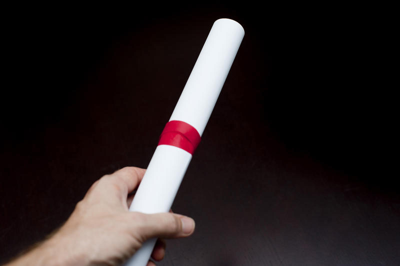 Man holding a graduation certificate in his hand rolled and tied with a red ribbon over a black background with copysapce conceptual of graduation and completing your studies and qualification