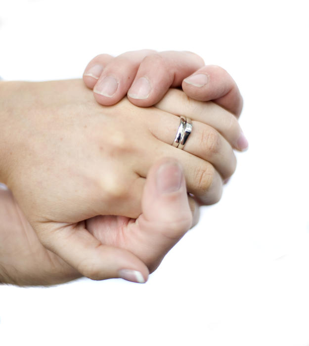 hands of a caucasian couple with hands crasped together and a wedding and engagement rings on display