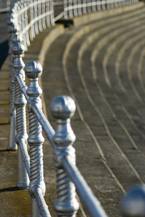 Curving silver painted old Blackpool Victorian balustrade bordering a road with steps leading up to it