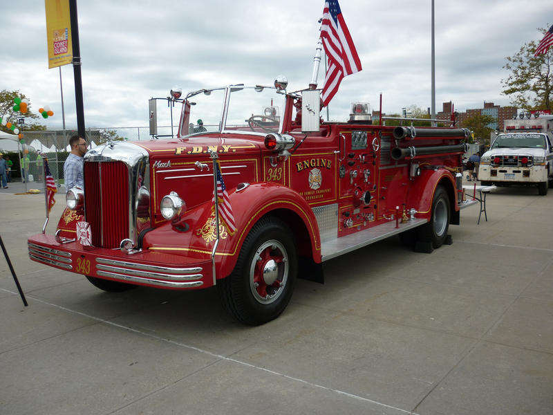 Fully restored historic red fire tender flying the American flag standing on a sidewalk being admired by a passerby