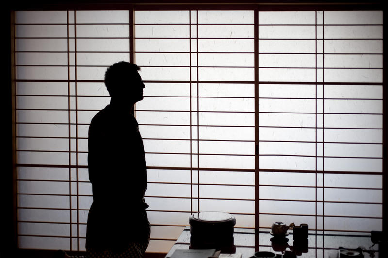 silhouette of a man wearing traditional japanese dress infront of a paper screen window