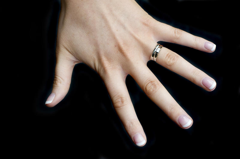 a caucasian female hand on a black background wearing wedding and engagement rings