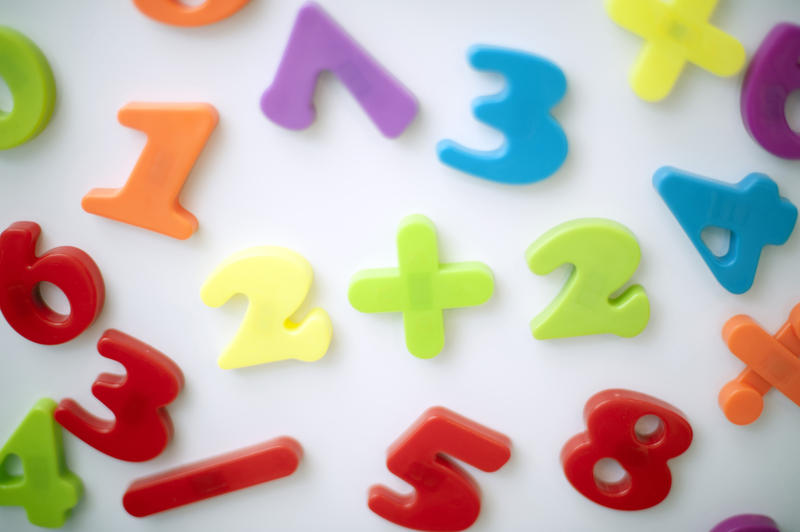 Learning maths with colourful plastic numbers and mathematical symbols scattered on a white background
