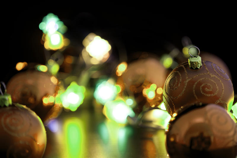 Festive Christmas lights shining across a reflective surface to baubles in the foreground with copyspace for your seasonal greeting