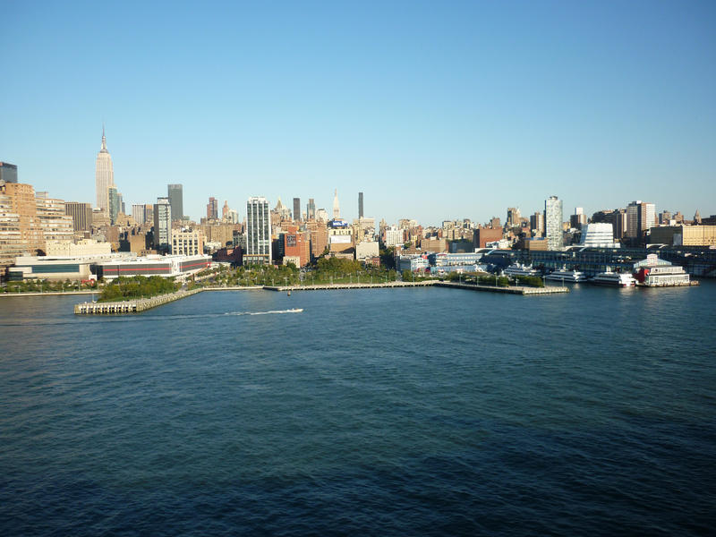 A view of the midtown Manhattan waterfront, skyscrapers and skyline shown from the Hudson river under a clear blue sky