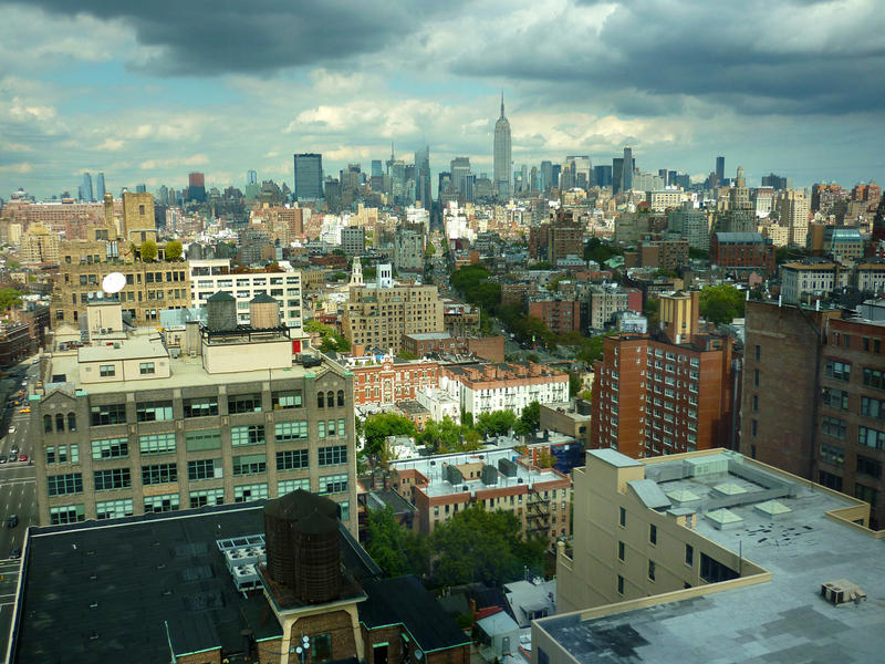 Panoramic view of Manhattan looking across highrise building to the skyscrapers of downtown New York silhouetted on the distant skyline under a cloudy blue sky