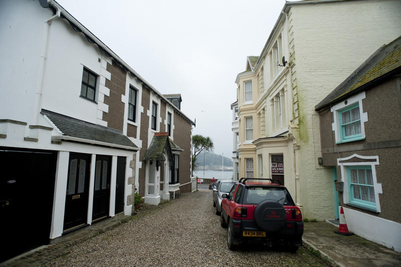 Street view in Marazion, Cornwall with a narrow cobbled street looking out towards the historical landmark of St Michael's Mount in the bay