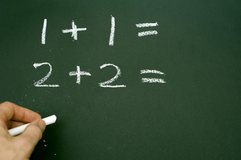 Hand writing simple mathematical sums on a chalkboard or blackboard in a kindergarten school teaching children basic addition