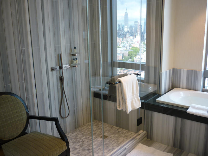 Modern apartment bathroom interior with a glass shower cubicle, basin and wonderful city view through the window