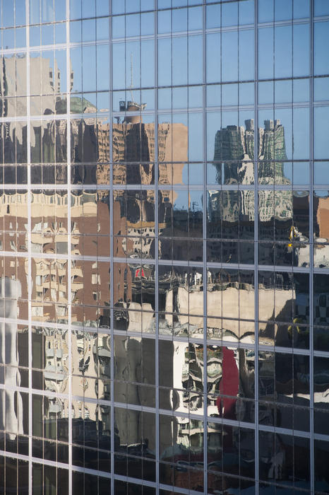 Reflections of urban buildings in the windows of a modern glass-fronted office block