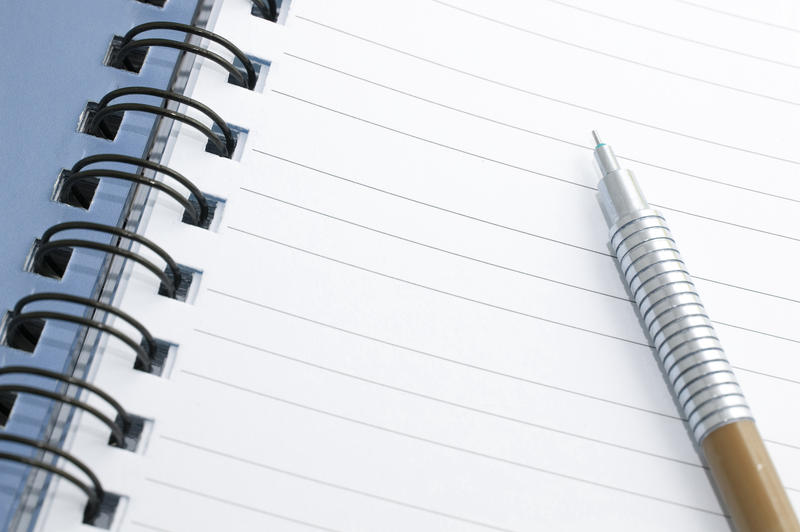 Silver metallic mechanical pencil lying on a notebook opened to a blank lined page