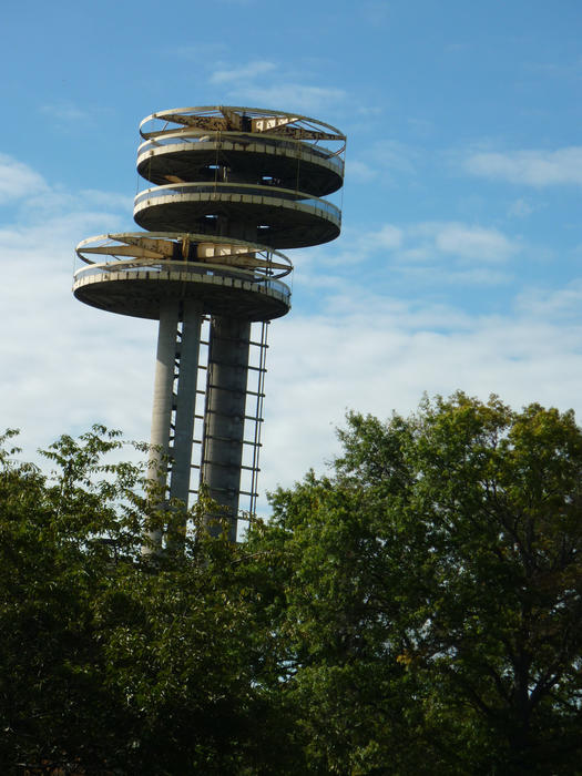 Ruins of a cylindrical observatory tower rising above green foliage high into a cloudy blue sky