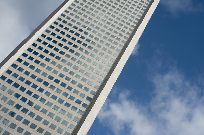 Angled view of the exterior facade of a modern city office block with multiple windows against a cloudy blue sky