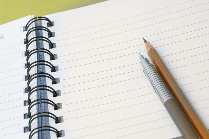 Office stationery ready for use with two pencils lying on a ringbound notebook open at a blank page with lines