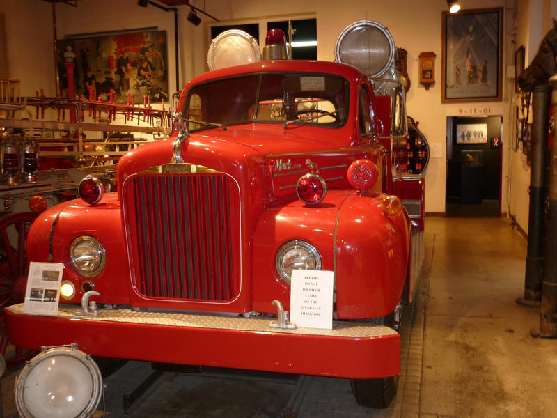 Beautifully restored old red fire truck on display in a museum with large spotlights mounted above the cab