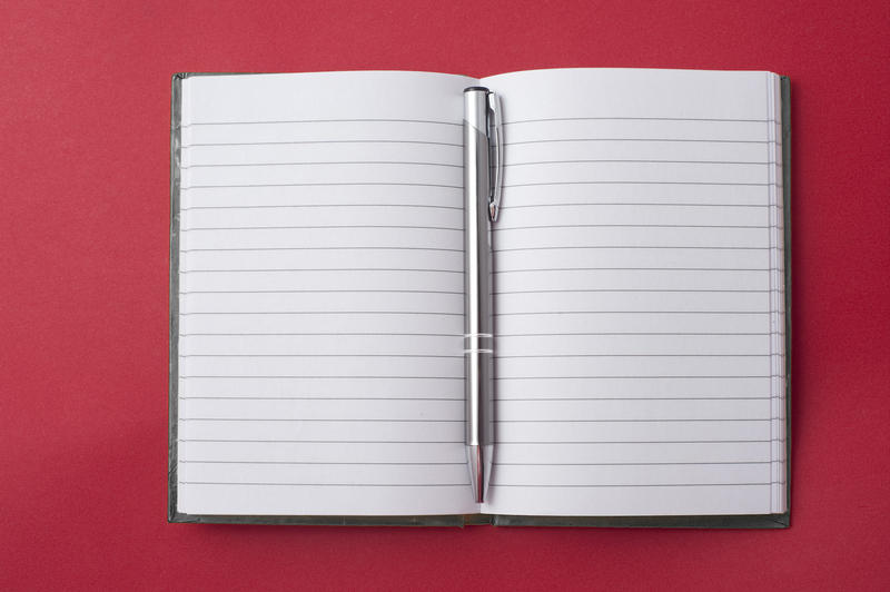 Opened blank lined notebook with a silver ballpoint pen in the centre ready for your message or text