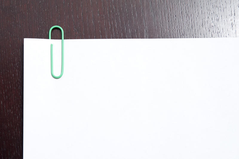 Blank document with several pages held together with a paper clip lying on a textured wooden surface
