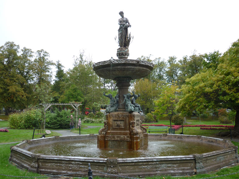 Beautiful figural fountain of a maiden pouring water in a formal leafy green garden in a park
