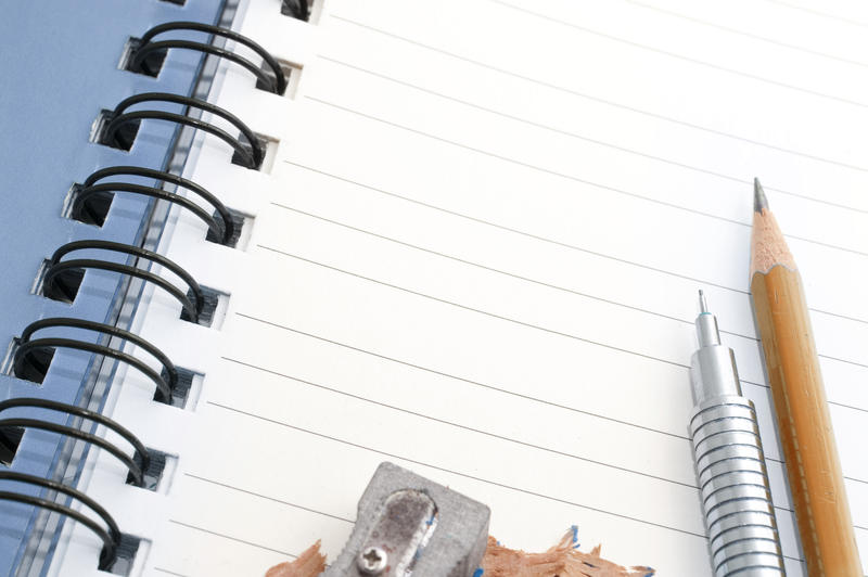 Mechanical and sharpened wooden pencils with a sharpener and shavings lying on a blank lined ringbound notebook