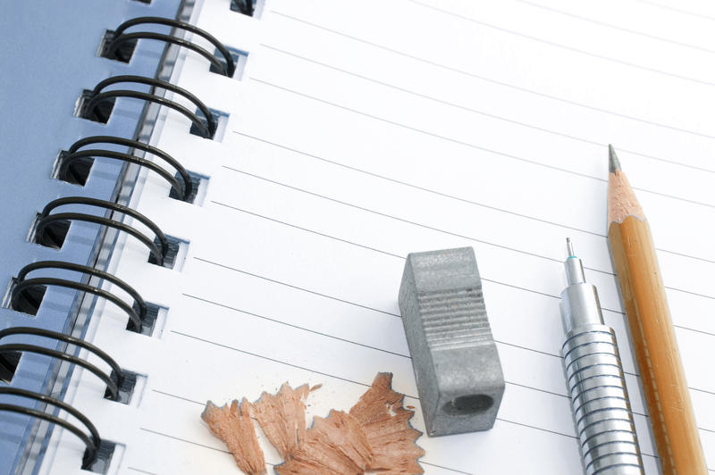 Pencils and pencil sharpener on an opened notebook with blank white lined pages ready for your text