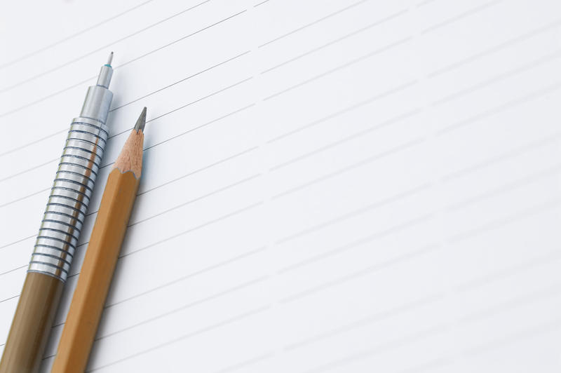 Two pencils, one mechanical and one sharpened wood, lying on a blank sheet of lined white paper