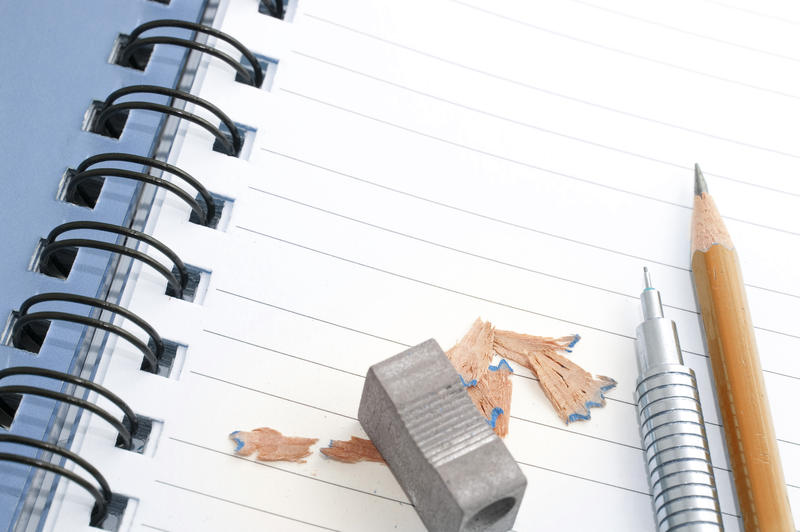 Two pencils, one mechanical and one wooden, lying on a blank notepad with a sharpener and shavings