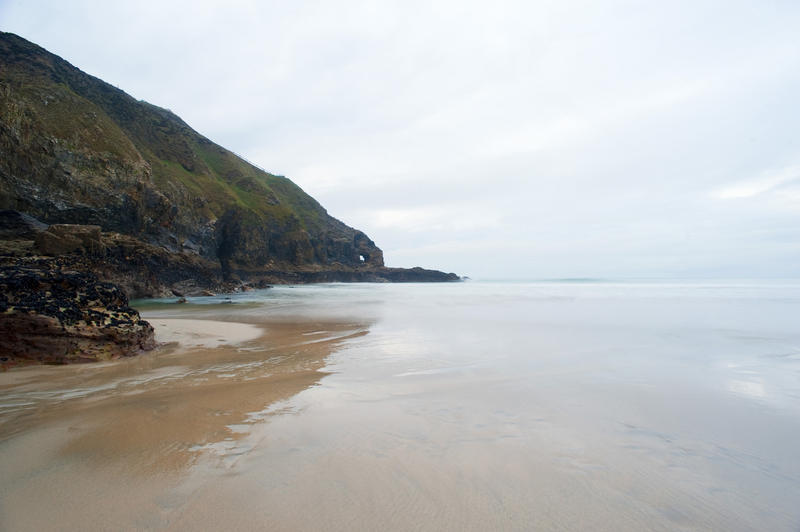 Headland reflected in wet sands from the incoming tide at Perran Beach, Perranporth, Cornwall