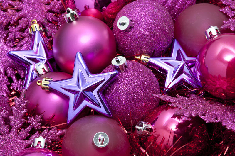 Seasonal background with a collection of pink Christmas bauble decorations and tinsel topped with purple stars