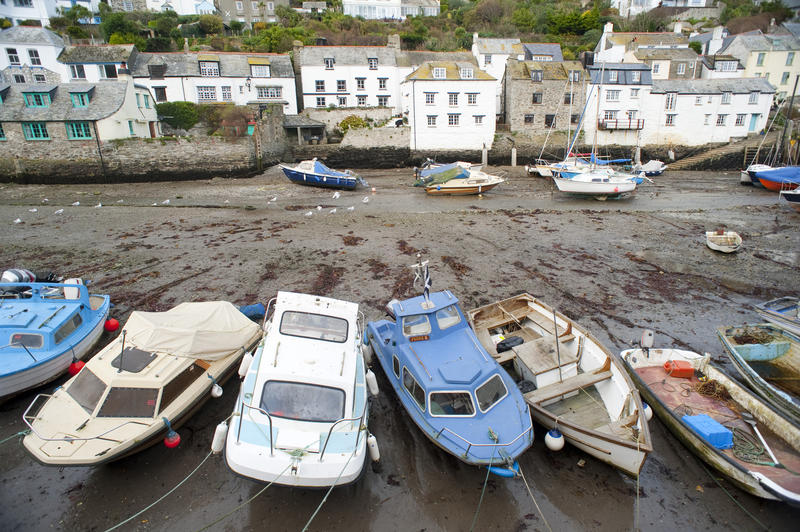 High angle view of a row of Polperro fishing boats beached on the sand by the receding tide with a row of white-washed fishermans cottages lining the waterfront of this popular fishing village behind