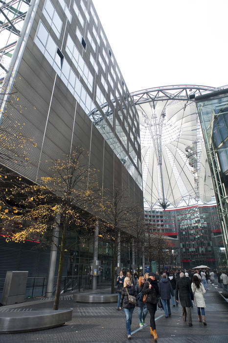 Crowds of people walking across Potsdamer Platz, Berlin towards the distinctive modern architecture of the conical glass roof on the Sony centre